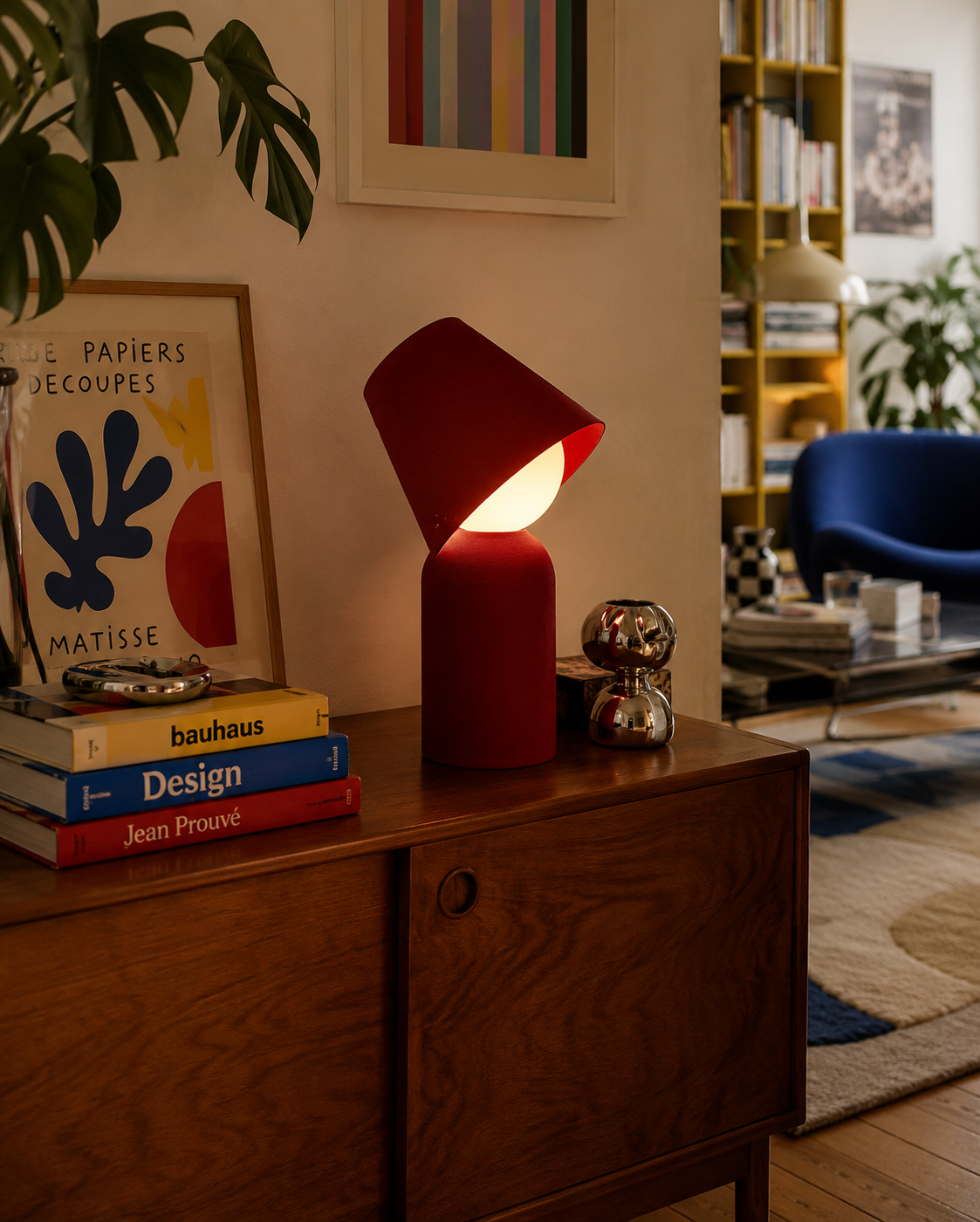 JUNEE red table lamp glowing beside design books in a warm contemporary interior.