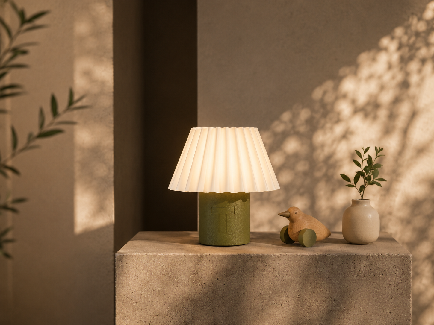 Firefly table lamp with a white pleated shade and olive base on a concrete surface.